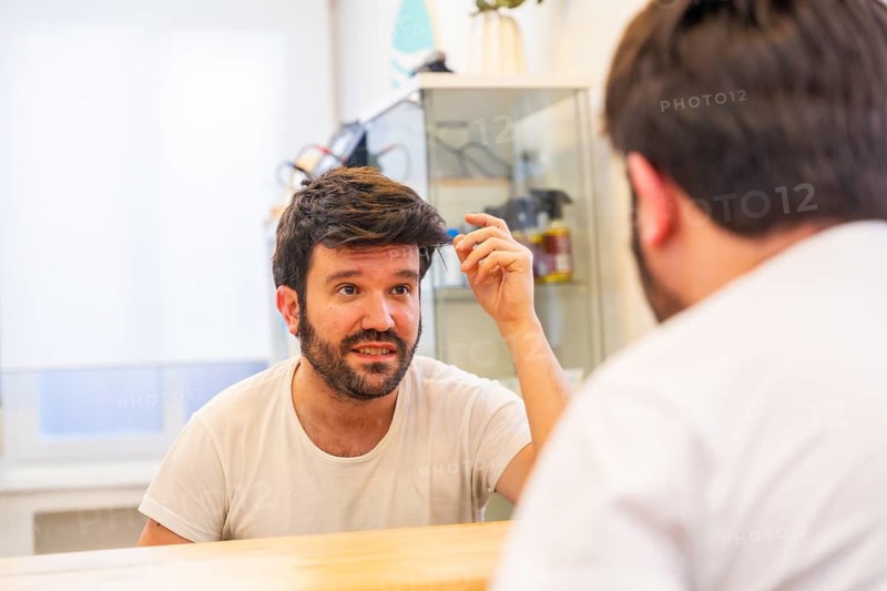 Happy bald man with a new capillary prosthesis looking into hair salon mirror