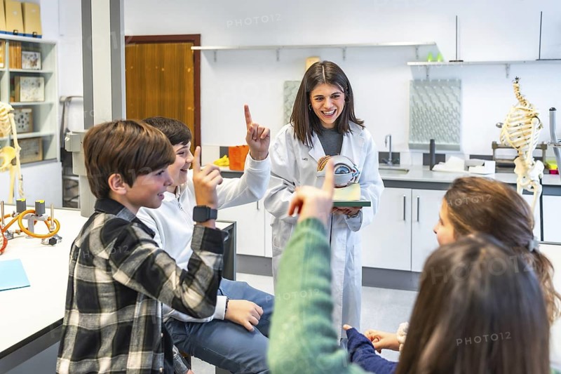 Middle school students participating in anatomy class, raising hands and learning about the human eye with a teacher and anatomical model
