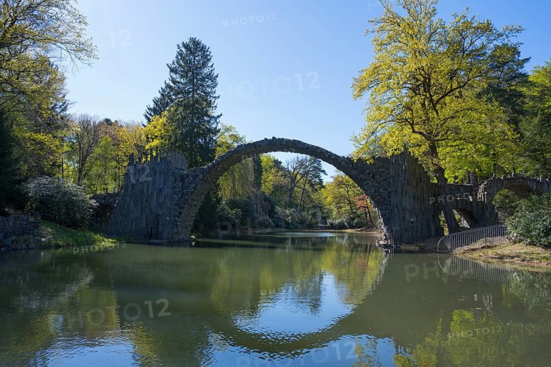 Stone bridge over quiet river with trees reflected in water on a sunny day, Rakotz Bridge, Devil's Bridge, Rakotzsee, arched bridge, reflection, basalt organ, Kromlau, Görlitz district, Saxony, Germany