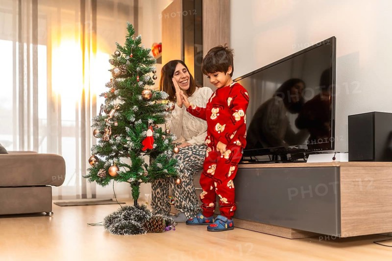 Happy mother and young son in pajamas smile and high five while decorating a festive christmas tree in their cozy living room, sharing warm holiday bonding and joy