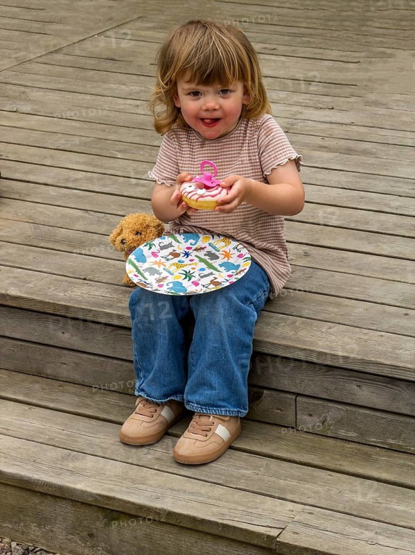 Little Caucasian girl, 3 years old, sitting on a wooden deck and eating a cake in Ystad, Skåne County, Sweden, Scandinavia