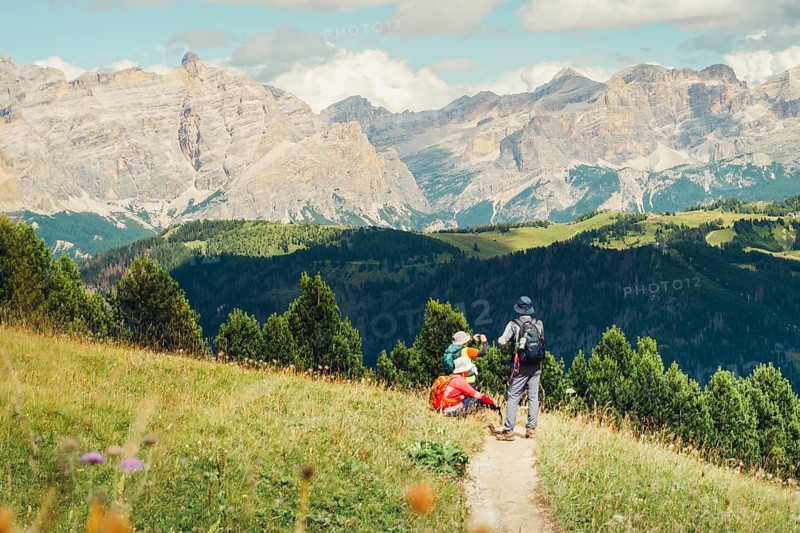 Middle-aged Asian group hikers hike trekking sunny italian Dolomites mountain trail.Alpine meadow landscape jagged peaks limestone rocks summer adventure travel exploration outdoors activity guide