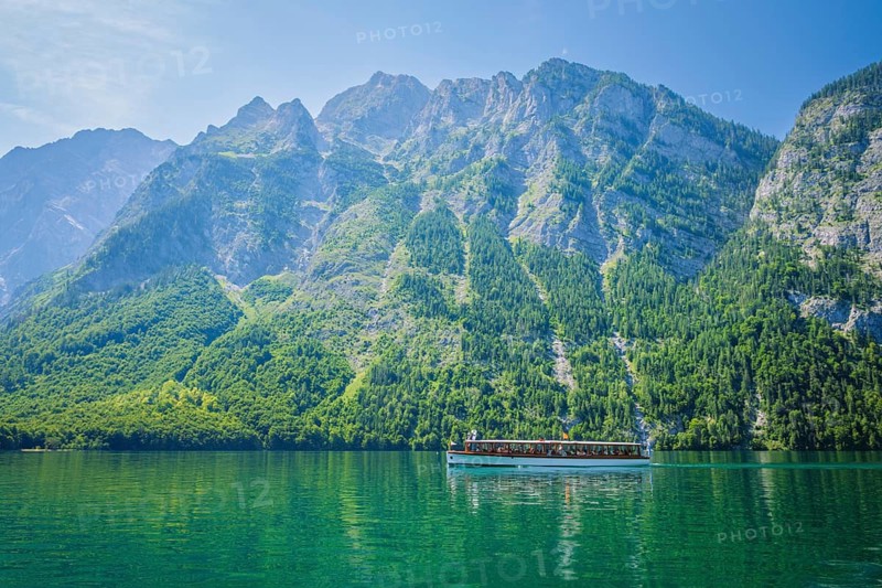 View of a tourist boat on the clear turquoise Konigsee lake, framed by the massive limestone mountains of Berchtesgaden National Park, Bavaria, Germany