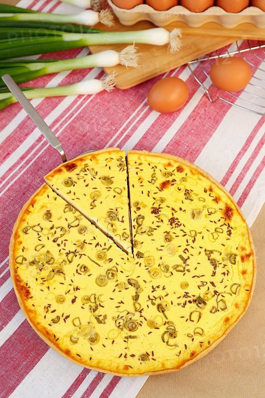 Swabian cuisine, salted cream cake with spring onions, hearty cake, salty shortcrust, baked, out of the oven, baked goods, spring onions, winter onions, cooling rack, cake rack, cake shovel, vegetarian, typical Swabian reinterpreted, baking, wooden stirring spoon, cooking spoon, eggs, fresh chicken eggs in egg carton, traditional cuisine, food photography, studio, Germany