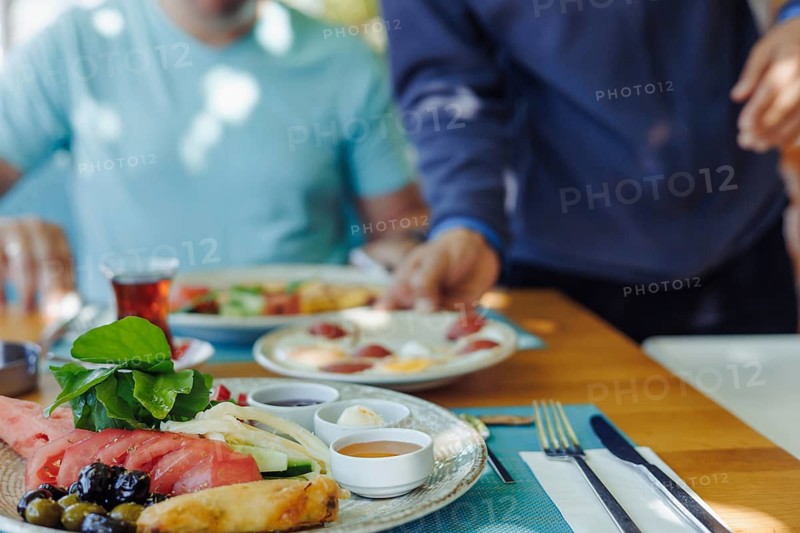 Group of friends shares a leisurely meal at a restaurant, enjoying various food and drinks. Waiter serves dishes in local traditional turkish style. Summer outdoor resort cafe, all inclusive concept