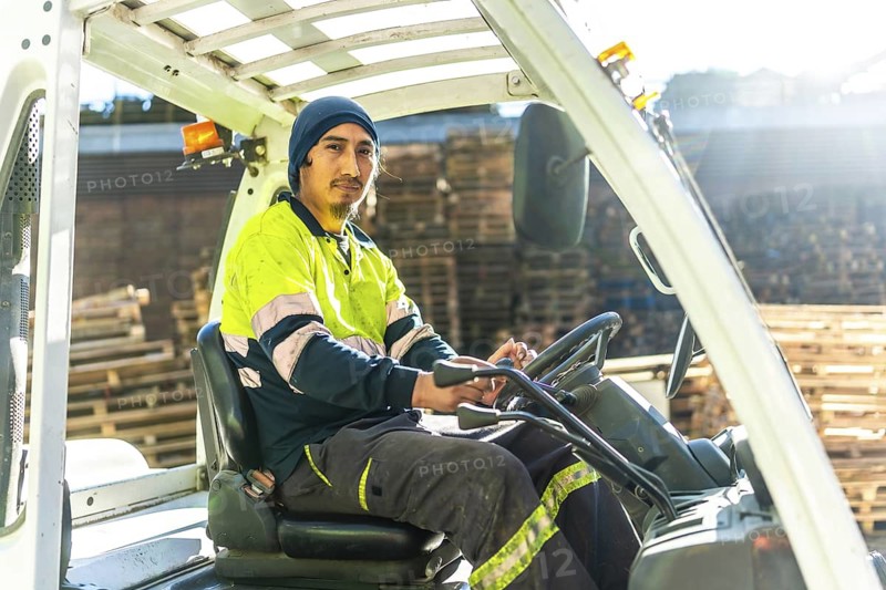 Rays of the sun illuminating a latin man worker driving forklift in a recycling plant