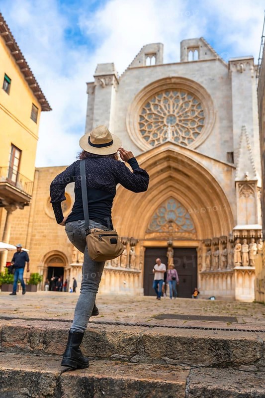Tourist climbing the steps of tarragona cathedral in catalonia admiring the rose window on a sunny summer day