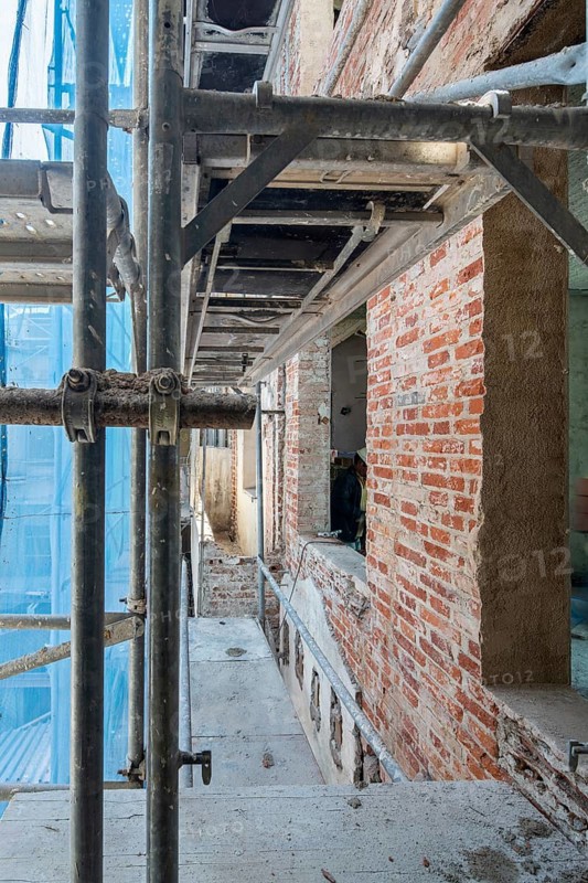 Scaffolding surrounds a building under renovation, showcasing exposed brickwork and construction materials in a dynamic urban setting, emphasizing progress and engineering