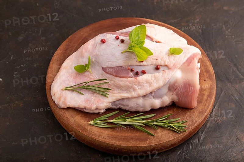 Raw Turkey Thigh with spices and rosemary on cutting board on black concrete background. side view, close up