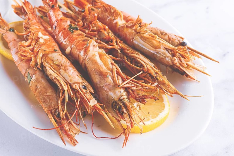 Freshly grilled prawns served, on a white platter, with lemon slices, for a delicious seafood experience