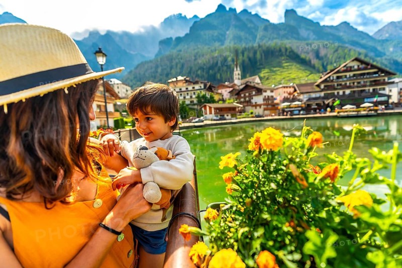 Mother holding her son enjoying the view of alleghe lake and civetta mountain range in the italian dolomites