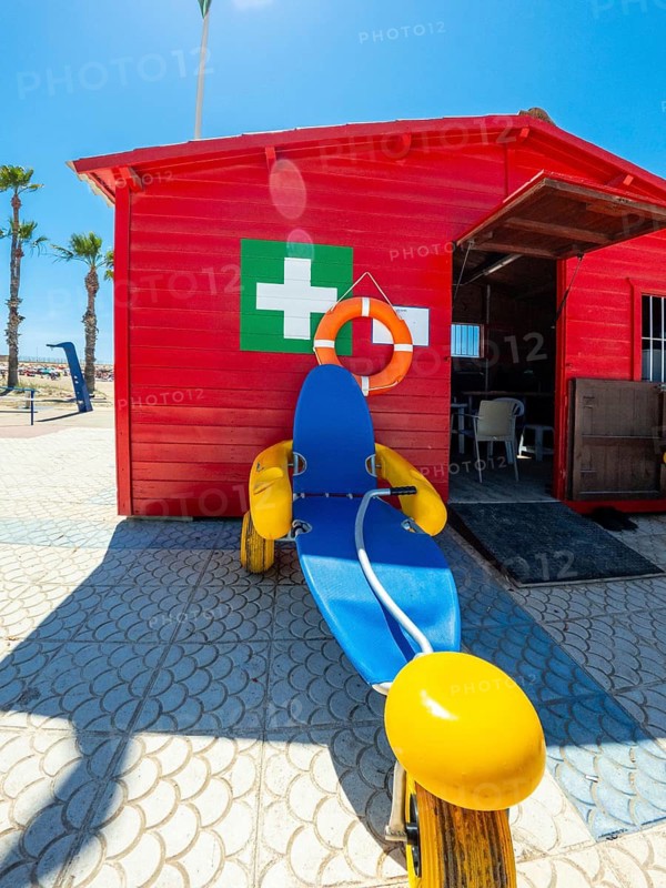 Floating wheelchair parked in front of a red lifeguard station on the beach, offering accessibility for people with disabilities