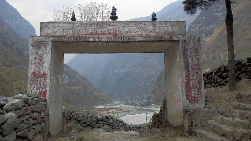 A stone gate with the inscription Welcome to Manang, overlooking a valley and a river, trekking at Annapurna Circuit, Manang, Nepal