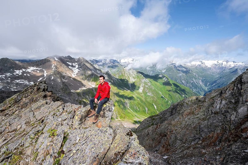 Mountaineer sitting on a rock, on a steep rocky ridge, on the summit of the Lasörling, view of the mountain panorama of the Venediger Group, Lasörling Group, Hohe Tauern National Park, East Tyrol, Tyrol, Austria