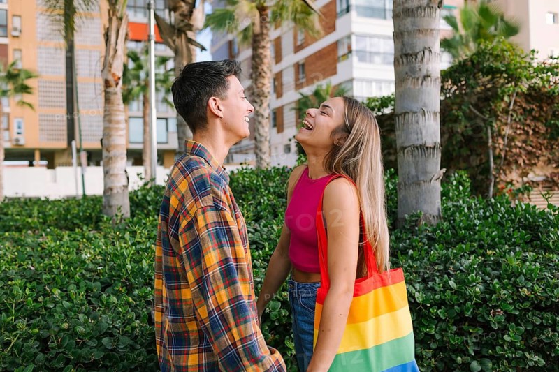 A happy lesbian couple shares a joyful moment outdoors, reflecting love and togetherness. With a rainbow tote, they celebrate pride and unity in a vibrant urban setting