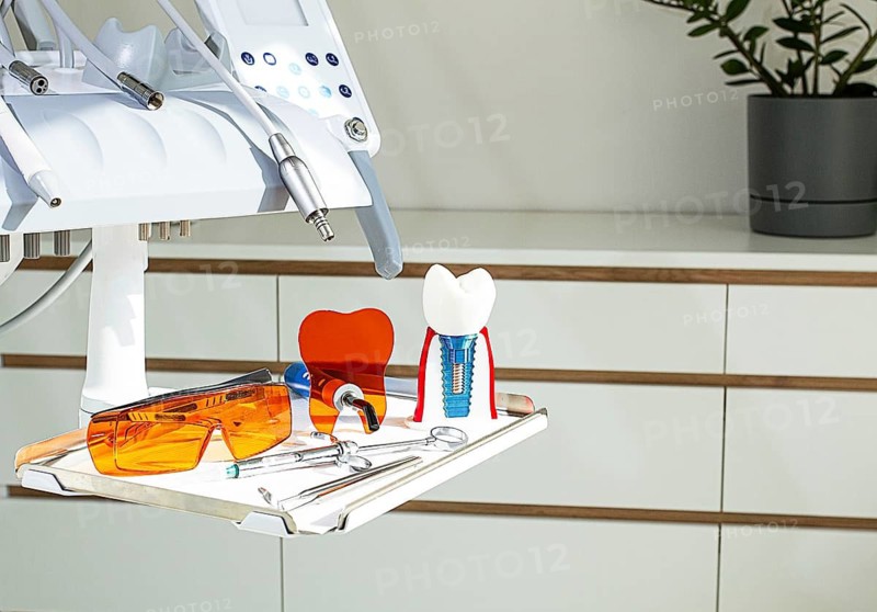 On the tray are various dental instruments, a model dental implant and bright orange safety glasses, ready for use in clinical dental settings