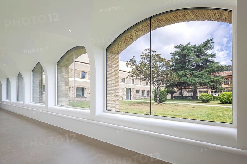 View os hospital through elegant arched windows in a bright corridor, overlooking a lush garden and classic building. The scene is serene, blending architecture with nature