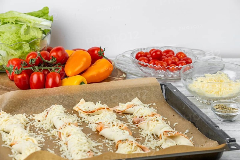 Pizza sticks on a tray sprinkled with grated cheese, surrounded by fresh ingredients, pizza