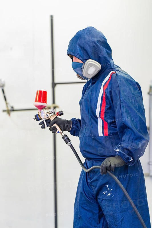 Person wearing blue protective clothing holds a spray gun in a paint shop, painter, Calw, Germany