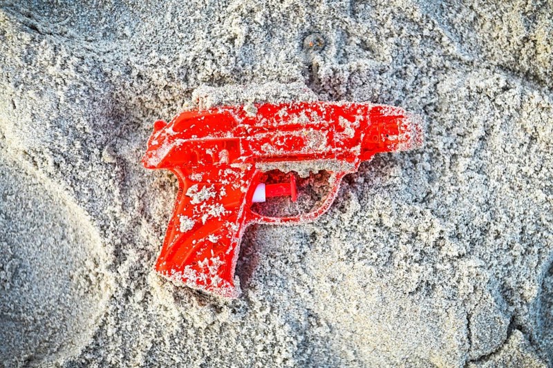 Red water pistol in the sand +++ editorial use only