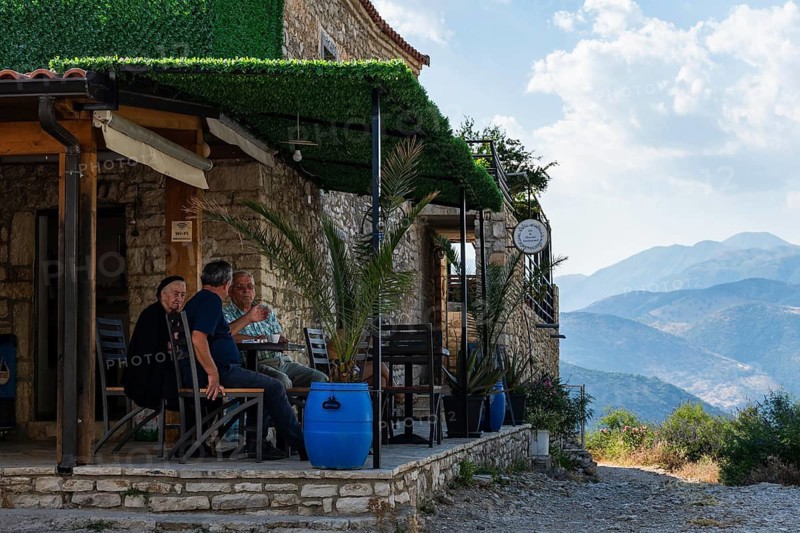QEPARO FUSHE, ALBANIA - JULY 28, 2026: People sitting at small stone café in Albanian mountains, real lifestyle travel illustration with scenic view and natural light