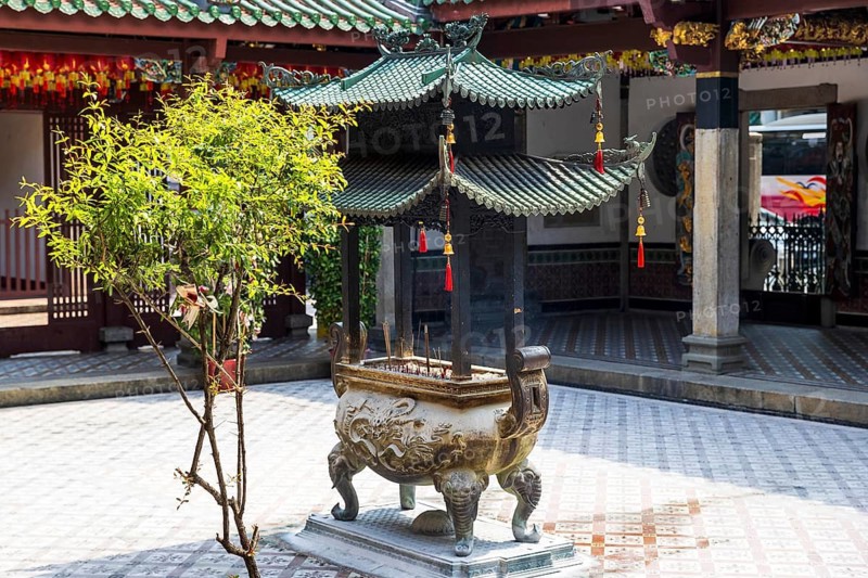 Smoking joss sticks rise from a dragon carved Bronze incense burner beneath a pagoda roof in the Thian Hock Keng Temple courtyard, Singapore