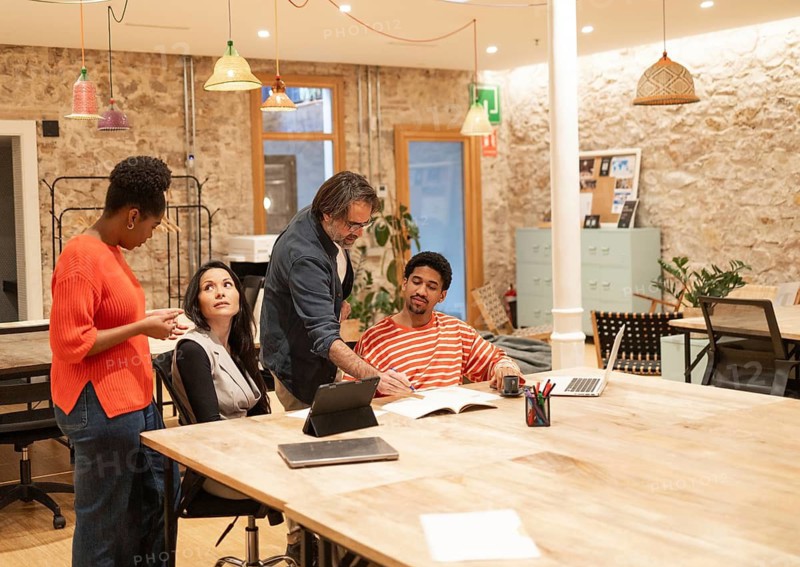 A diverse group of professionals engages in discussion in a modern coworking space The open layout, creative lighting, and natural elements foster collaboration and creativity