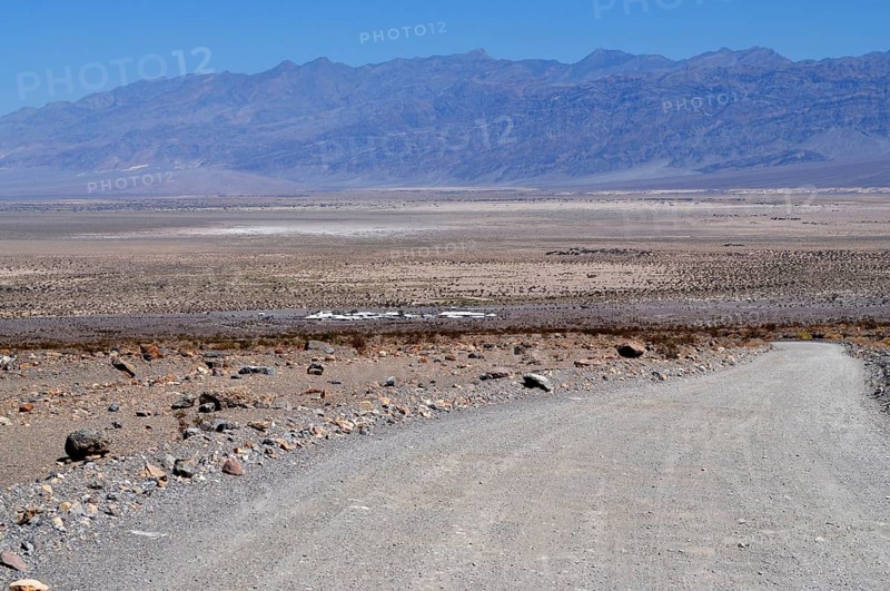 Gravel road leads into the dry, wide plain with mountains in the background, Death Valley National Park, Mojave Desert, California, Nevada, USA