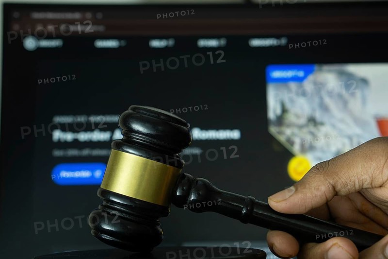 Dhaka, Bangladesh- 20 June 2025: A hand holds a gavel in front of a computer screen displaying Ubisoft's website