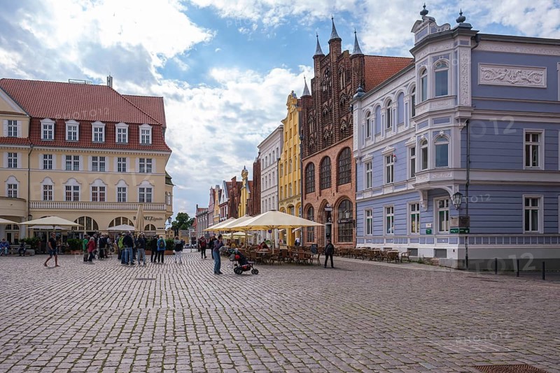 Historic city view with cobblestone square surrounded by old buildings and cafés under cloudy sky, Stralsund, Mecklenburg-Western Pomerania, Germany