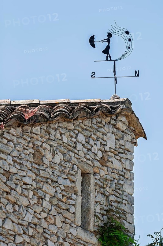 Weather vane on a stone roof under a blue sky, Provence, France