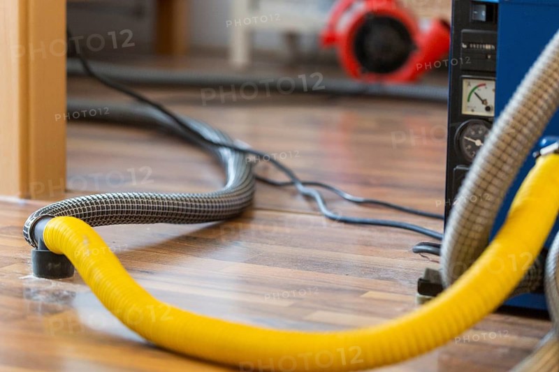 Professional water damage repair Drying equipment and hoses for underbody drying on wooden floor laminate
