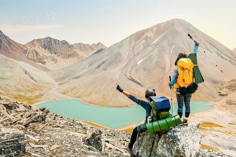 Aerial rising view young woman Hiker standing and watching beautiful alpine lake and mountains in country Georgia. Kazbegi, Kelitsadi lake, Georgia