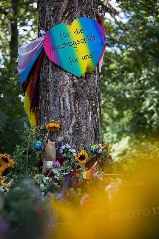 Sign bound around a tree with the text For attack victims - for us at an improvised memorial made of flowers and candles at the Tatort in Berlin's Tiergarten on 29.07.2026. During the closing Christopher Street Day rally on July 25, 2026, a gunman with a van in Berlin's Tiergarten killed at least one participant and injured several others, some seriously