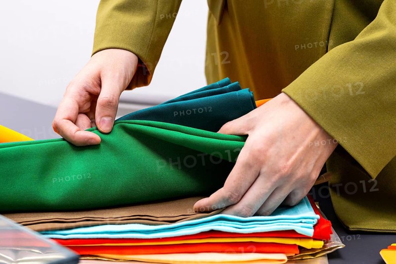 An image consultant arranges a variety of colorful fabrics during a consulting session. The professional adjustment highlights the importance of color and texture in creating a personalized style