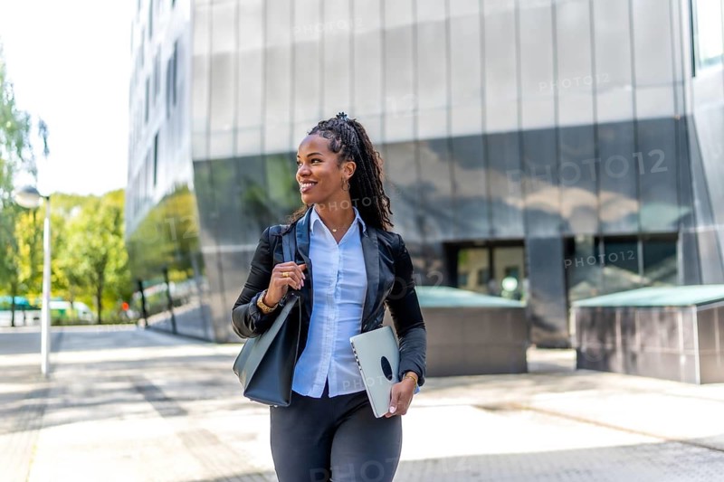 Pretty latin businesswoman walking holding laptop and handbag in a financial district