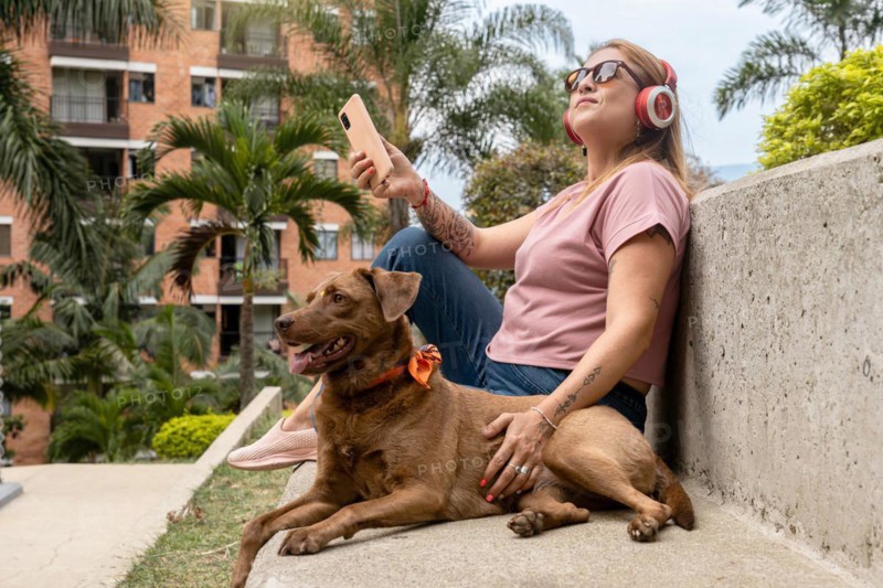 Middle-aged woman enjoying outdoors and listening to music, accompanied by her pet in the tropical city
