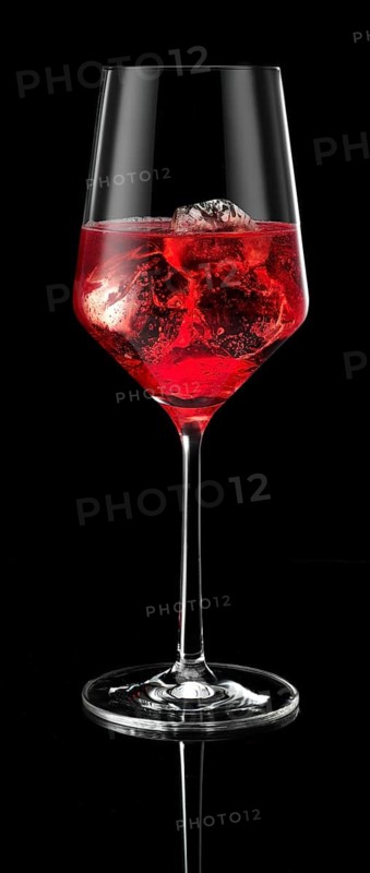 Wine glass filled with ice cube cubes and cocktail in front of a black background, studio shot