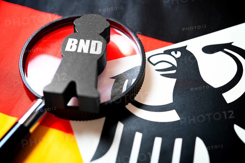 Spy figure with inscription BND and magnifying glass on federal eagle and German flag, symbolic photo German secret service reform, photo montage +++ editorial use only