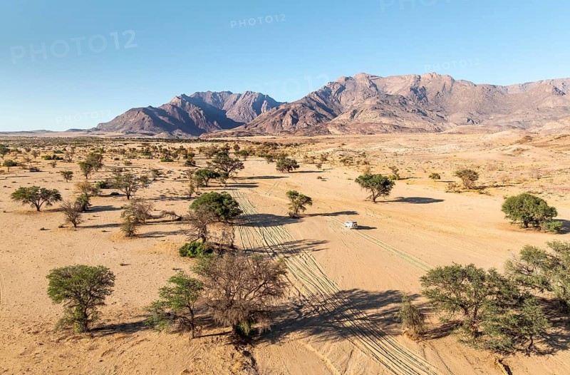 Aerial view of off-road car driving in dry riverbed and desert landscape on the Ugab River, behind Brandberg, Erongo, Damaraland, Namibia