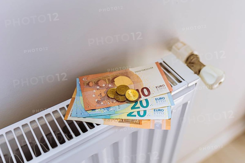 Euro banknotes and coins on radiator during winter heating season. Concept of rising household energy bills, expensive home heating, cost of living crisis and increasing utility expenses in Europe