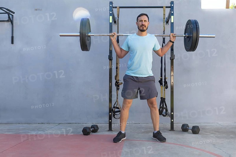 Sportsman performing a back squat with a barbell in an outdoor gym, showcasing strength and commitment to fitness while embracing an active lifestyle under the summer sun