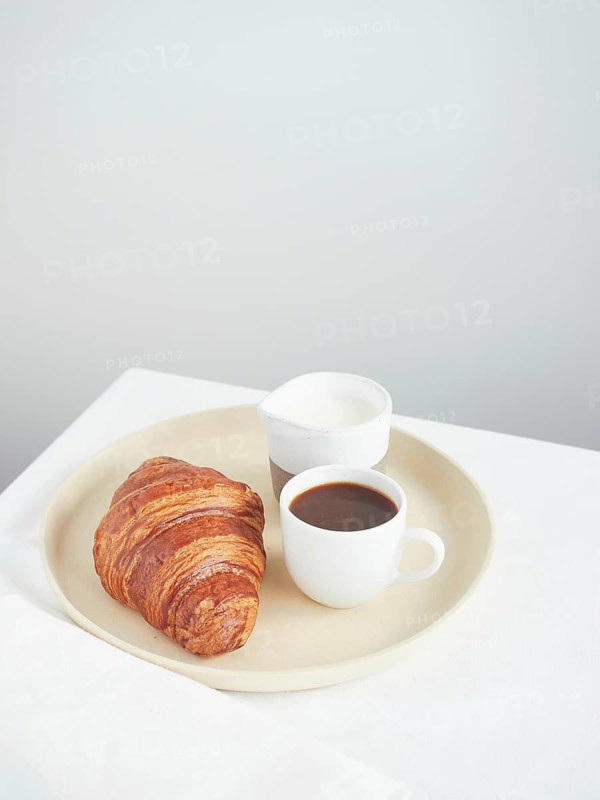 Simple continental breakfast on the table croissant, coffee cup and milk jug