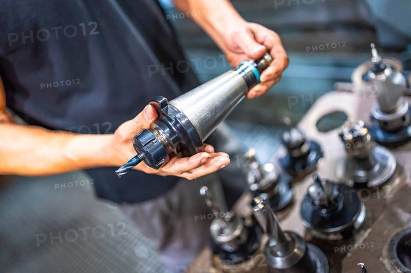 Close-up photo of the hands of a male worker holding the head of a milling machine in a cnc factory