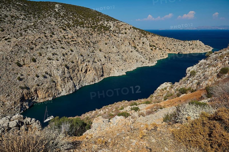 A secluded rocky bay with deep blue water and a hidden boat, Rina, harbour, Vathi, Vathys, Kalymnos, Dodecanese, Greek Islands, Greece