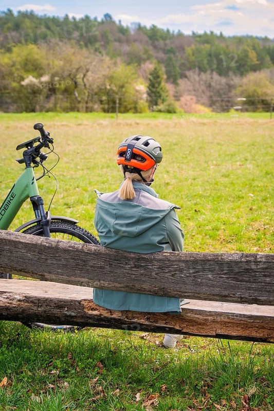 Person sitting on a bench at the edge of the forest, next to a bicycle, spring-like weather, e-bike, Gechingen, Heckengäu region, Germany