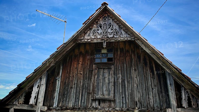 Close-up of an old wooden gable of a traditional wooden house with antenna under blue sky, Croatia