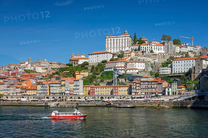 Tourist boat crosses the Douro River in Porto, Portugal, below Ribeira riverfront and the historic hillside cityscape
