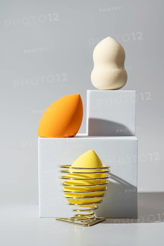 A visually appealing display of cosmetic sponges, including vibrant orange and yellow, arranged on geometric white blocks Ideal for beauty and makeup themes
