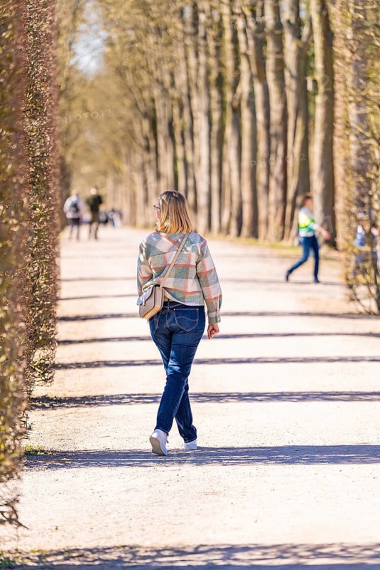 Woman walking along a tree-lined path. Spring mood and relaxed atmosphere in sunny weather, Schwetzingen Palace Gardens, Germany